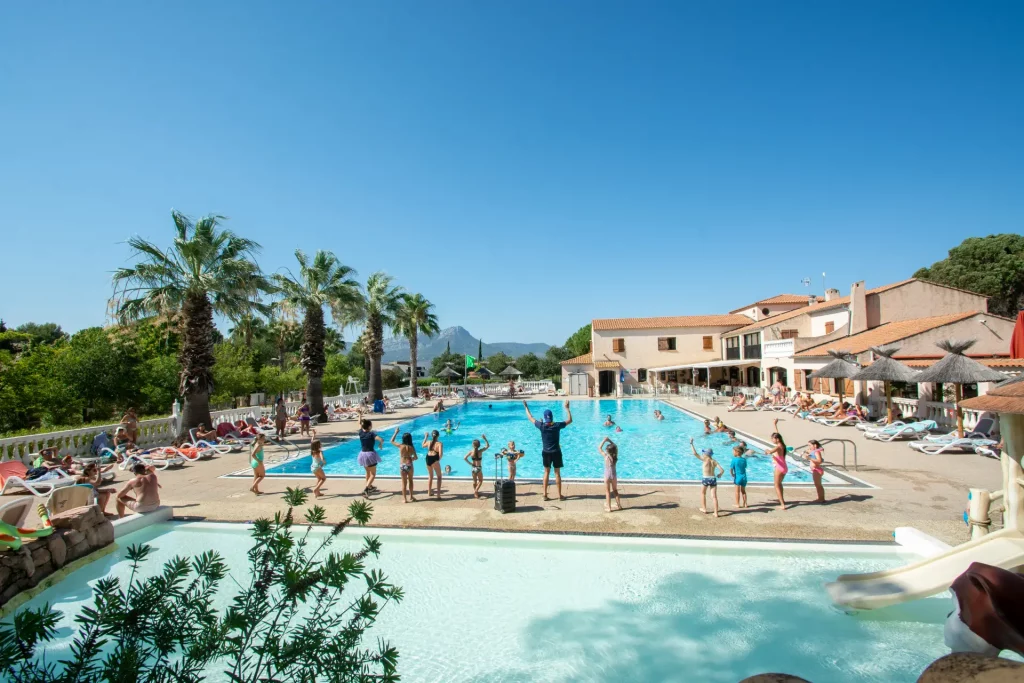 Piscine extérieure ensoleillée avec palmiers et vacanciers.