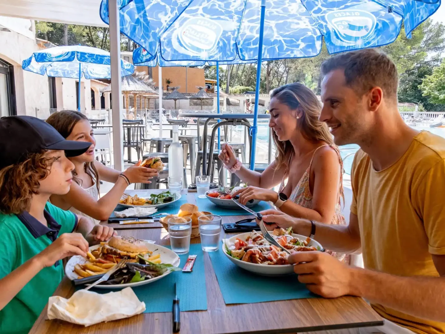 Famille déjeunant ensemble en terrasse au bord de piscine.